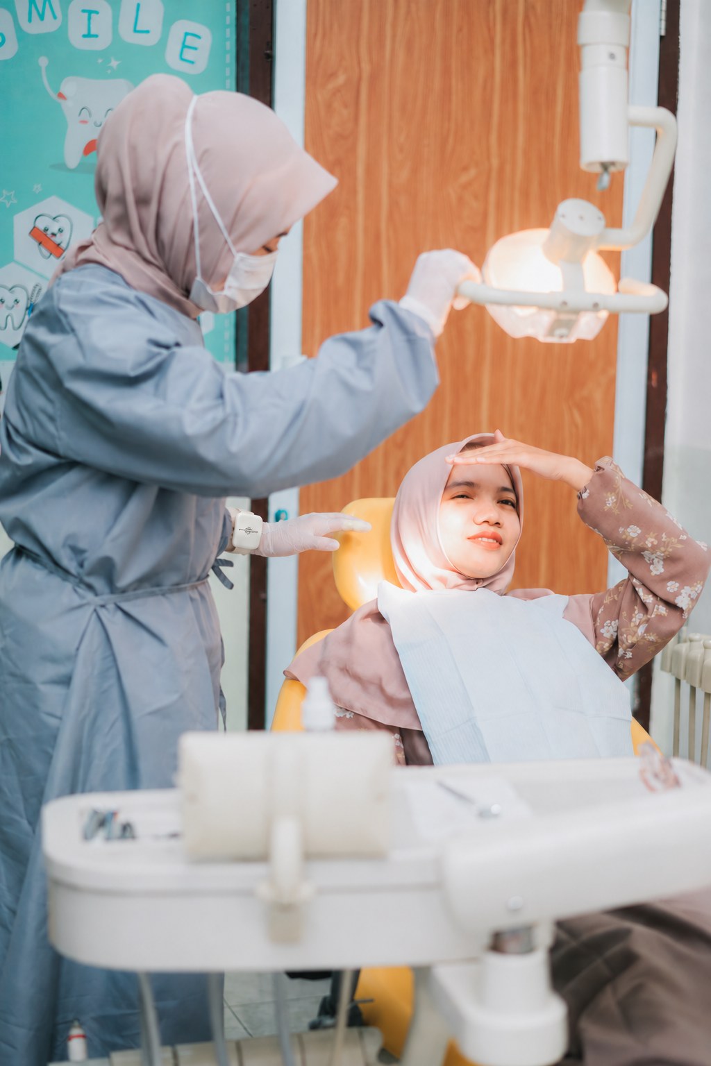 Suasana klinik gigi saat dokter menyesuaikan lampu dental, perangkat pada pergelangan diedit ke versi 2026